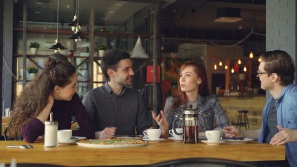 In einem kleinen Café oder Pizzahaus plaudert und lacht eine fröhliche und attraktive Gruppe weiblicher und männlicher Freunde miteinander. Kommunikations- und Foodservice-Konzept. — Stockvideo