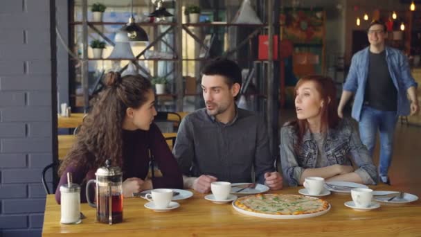 Knappe jonge kerel in casual denim kleding is het ontmoeten van zijn vrienden in café laat komen en zijn vrienden met hoge vijf groet. Vriendschap en begrip eten. — Stockvideo