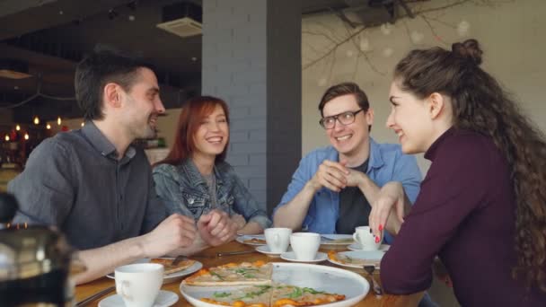 Knappe studenten gaat lachen doen high-five en gebaren tijdens een diner eten van pizza in café. Gelukkige mensen, communicatie en heerlijke maaltijd concept. — Stockvideo