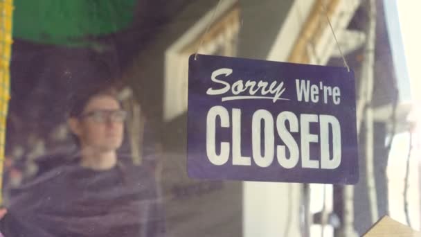 Attractive male waiter in apron is changing doorplate from "sorry we are closed" to "yes we are open". Beginning new work day, employee and business concept. — Stock Video