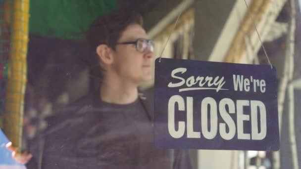 Cheerful cafe employee in apron is changing doorplate from "sorry we are closed" to "yes we are open". Starting new work day, waiter and business concept. — Stock Video