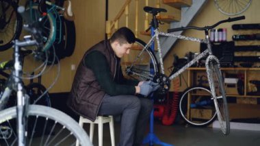 Dolly dışkı çalışma alanı'ndaki modern bisiklet yanında oturan kırık bisiklet pedalla sabitleme odaklı genç machanic bir kadeh. Bakım, meslek ve insanlar kavramı.
