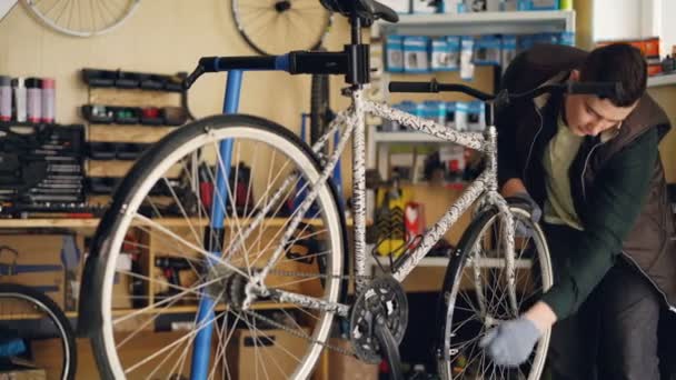Skilled repairman is concentrated on repairing bicycle wheel fixing it with professional wrench while working in small workshop. Maintenance and people concept. — Stock Video