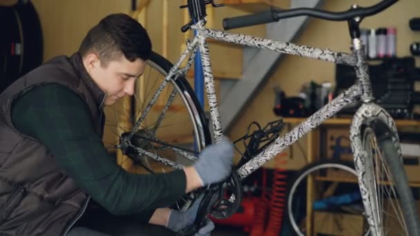 Dollly Shot von konzentrierten jungen Reparateur Reparatur kaputten Fahrrad Lauffläche sitzt in der Nähe moderner Fahrrad am Arbeitsplatz. Wartungs- und Personalkonzept. — Stockvideo