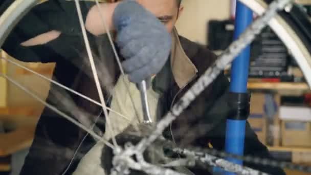 Professional bike repairman is busy fixing mechanism of bicycle wheel rotating it and adjusting with wrench. Metal wheel spokes are turning in foreground. — Stock Video