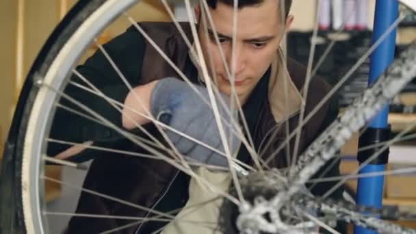 Cara concentrada hábil mecânico está reparando roda de bicicleta com chaves enquanto trabalhava em seu local de trabalho. Manutenção de bicicletas, pessoas e conceito de profissão . — Vídeo de Stock