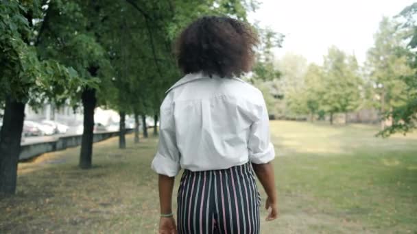 Медленное движение красивой афро-американской леди, идущей на улицу в парке поворачивая — стоковое видео
