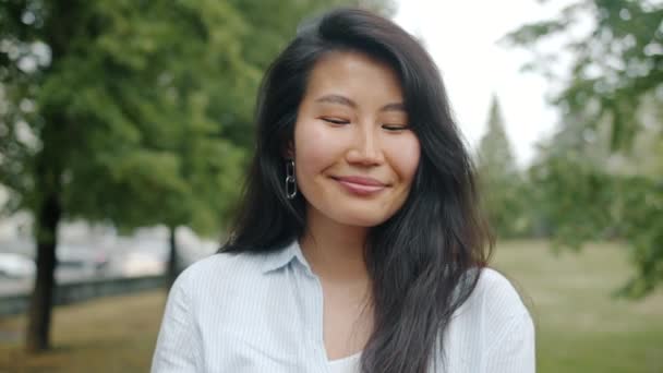 Słodkie Azji dziewczyna uśmiechnięty flirt patrząc na aparat fotograficzny w park w letni dzień — Wideo stockowe