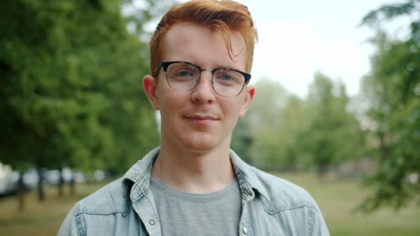 Portrait of handsome student starting to smile standing in city park alone — Stock Video
