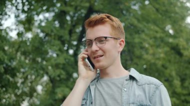 Şehir parkında cep telefonuyla konuşan gözlüklü çekici bir işadamı.