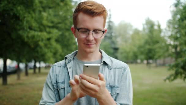 Νεαρός που χρησιμοποιεί smartphone στο πάρκο συγκινητική οθόνη απολαμβάνοντας σύγχρονη συσκευή — Αρχείο Βίντεο