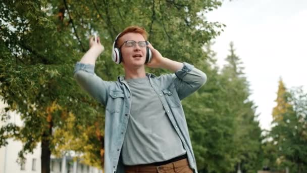 Slow motion van man in hoofdtelefoon dansen zingen buiten met smartphone — Stockvideo