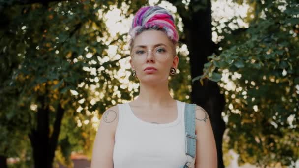 Portrét roztomilé dívky hipster s obarvenými vlasy, piercing a tetování v městském parku — Stock video