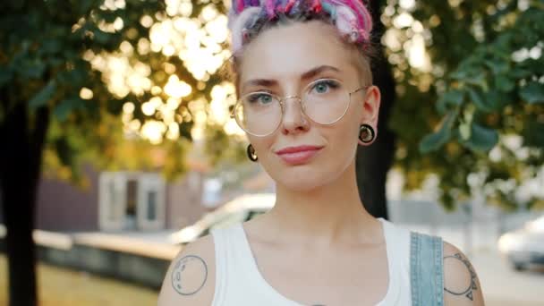 Slow motion of stylish girl with piercing, tattoo, colorful hair smiling in park — Stock Video