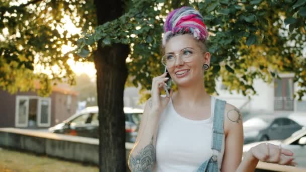 Dövmeli ve renkli saçlı bir kız şehir parkında cep telefonuyla konuşuyor. — Stok video