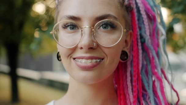Cámara lenta de chica con frenos dentales sonriendo mirando a la cámara en el parque de la ciudad — Vídeos de Stock
