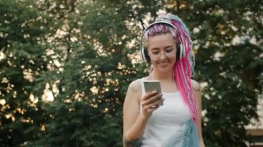 Dışarıda dans eden akıllı telefonlu neşeli genç bir kadın. Kulaklık takıyor.