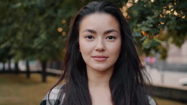 Retrato de cerca de una bonita estudiante asiática sonriendo sola en el parque urbano — Vídeos de Stock