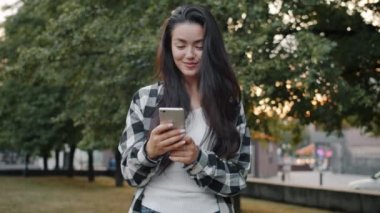 Parkta akıllı telefon kullanan Asyalı hippi ekranlara dokunup modern aletlerin keyfini çıkarıyor.