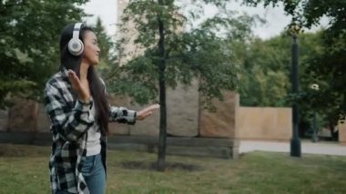 Şehir parkında kulaklıkla dans eden Asyalı kadının ağır çekimde