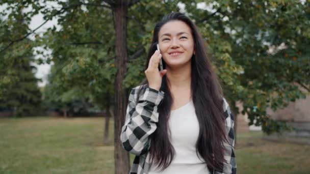 Alegre Asiática dama charlando en el teléfono celular en verde parque en verano al aire libre . — Vídeo de stock