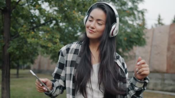 Estudiante asiático guapo disfrutando de la música en auriculares bailando al aire libre — Vídeo de stock