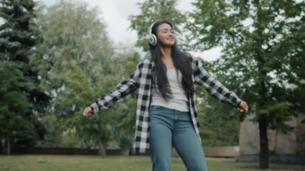 Veselý asijské žena tanec v parku v létě na sobě sluchátka baví — Stock video