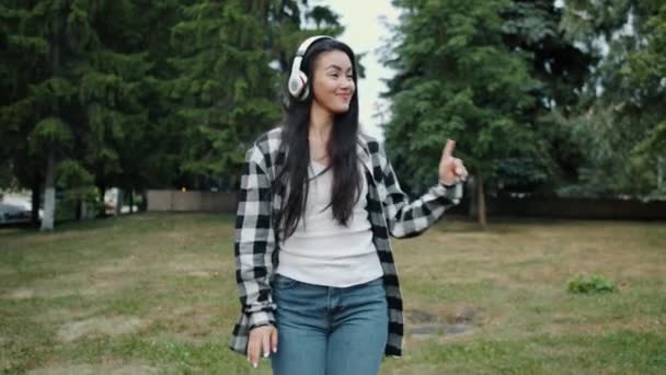 Cámara lenta de joven asiática dama en auriculares bailando en parque urbano solo — Vídeos de Stock