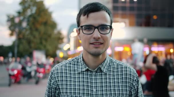 Boldog fickó szemüvegben mosolyogva áll a sétálóutcában a modern városban — Stock videók