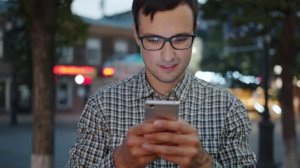 Красивий хлопець, використовуючи смартфон, торкаючись екрана на вулиці міста ввечері — стокове відео
