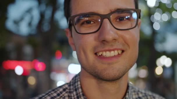 Крупним планом портрет щасливої молодої брюнетки в окулярах, стоячи на відкритому повітрі ввечері — стокове відео