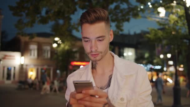 Cámara lenta del estudiante usando la pantalla táctil del teléfono inteligente al aire libre por la noche — Vídeos de Stock