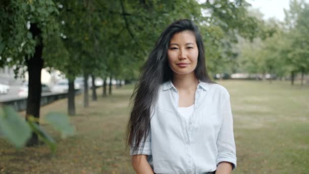 Портрет привлекательной азиатки, улыбающейся, стоя в зеленом парке в одиночестве летом — стоковое видео