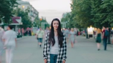 Mutlu bir gülümsemeyle şehir caddesinde duran genç bir bayanın hızlandırılmış portresi.