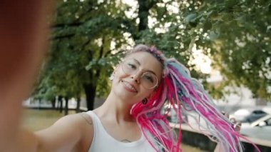 Benzersiz saç stili olan sevimli bir kadın dışarıda fotoğraf çekiyor ve kameraya bakıyor.