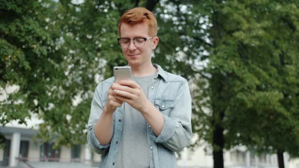 Весела людина торкається екрану смартфона на відкритому повітрі в міському парку, що стоїть один — стокове відео