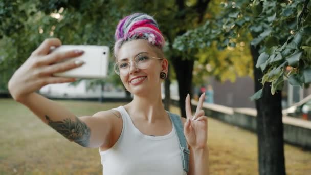 Trendig ung dam som tar selfie i stadsparken poserar med handgester ler — Stockvideo