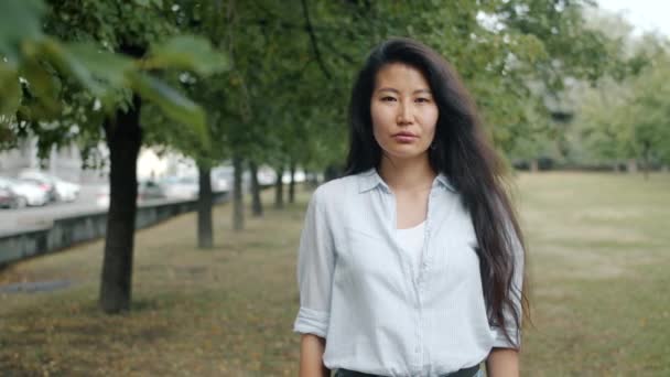 A városi parkban álló komoly, fiatal ázsiai üzletasszony portréja — Stock videók