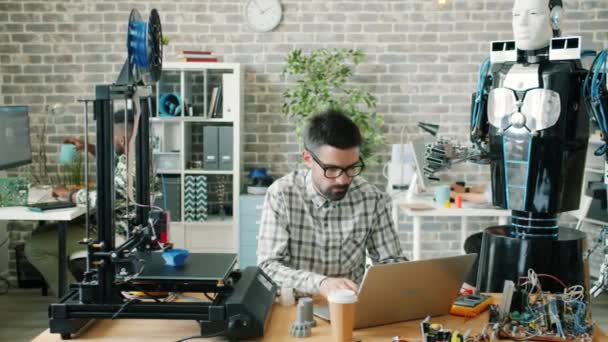 Jovem cientista do sexo masculino trabalhando com robô, laptop e impressora 3d no local de trabalho — Vídeo de Stock