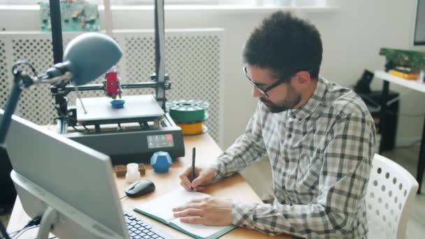 3D 프린터가 플라스틱 모양을 모델링 하는 동안 컴퓨터와 함께 일하는 잘생긴 남자 — 비디오