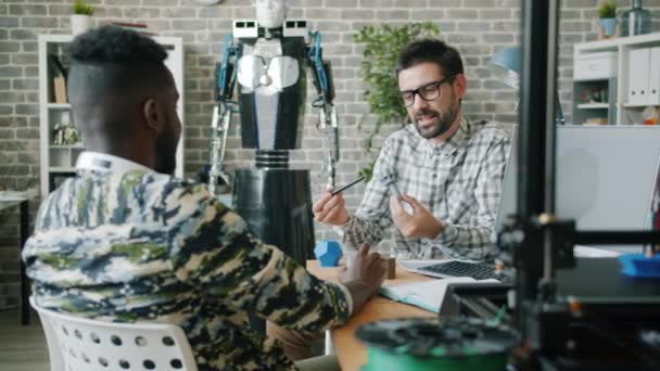Jóvenes empresarios discutiendo detalles impresos 3d para robot moderno en la oficina — Vídeos de Stock
