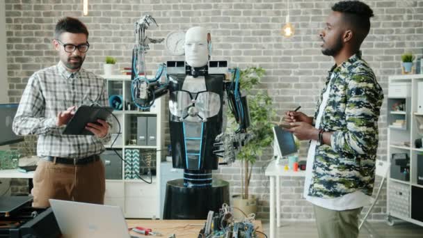 Jovenes alegres probando robot con tableta trabajando juntos en la oficina moderna — Vídeos de Stock