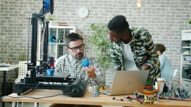 Chers collègues jeunes hommes parlant au bureau en utilisant une imprimante 3D, une tablette et un ordinateur portable — Video