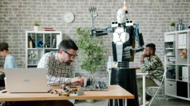 Ofiste robot yapan mühendis işine odaklanmış, bilgisayar kullanan meslektaşlar