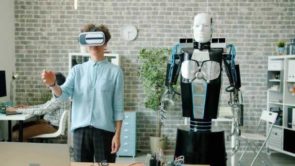 Розумний робот рухає руку, як молода жінка в окулярах віртуальної реальності в офісі — стокове відео