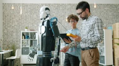 Modern ofiste insan benzeri robotu tablet kullanarak test eden geliştiriciler.