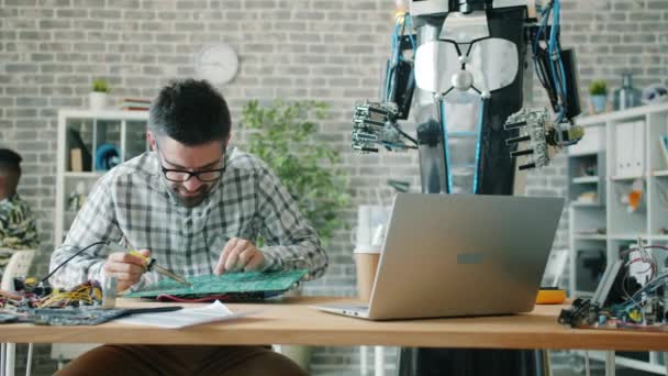Robotics engineer guy using soldering iron to fix microcircuit in workroom — Stock Video