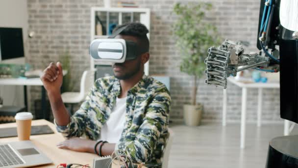 Robot ve sanal gerçeklik gözlüklü Afro-Amerikan adam el ele hareket ediyor. — Stok video