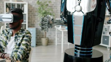 AR gözlüklü Afro-Amerikalı adam iş yerinde el ele hareket eden robotu test ediyor