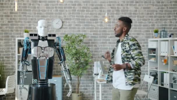 Радостный афроамериканец танцует с человекоподобным роботом в офисе и веселится. — стоковое видео